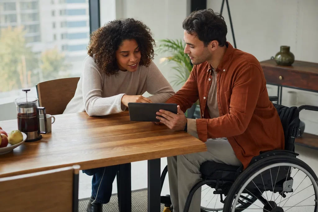 Two adults comparing accessible venue options together at a home table; one adult uses a wheelchair.