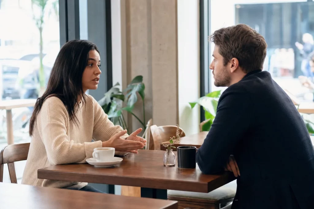 Two adults having a brief, respectful closing conversation in a public café with calm posture and personal space.
