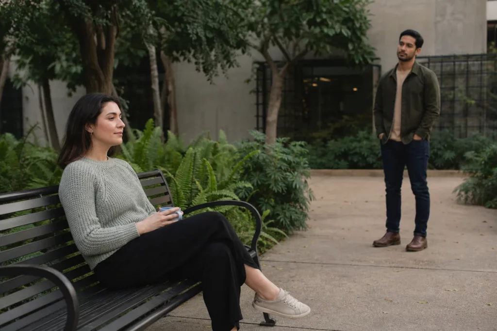 An adult taking a quiet grounding pause outdoors while their partner waits nearby without crowding them.