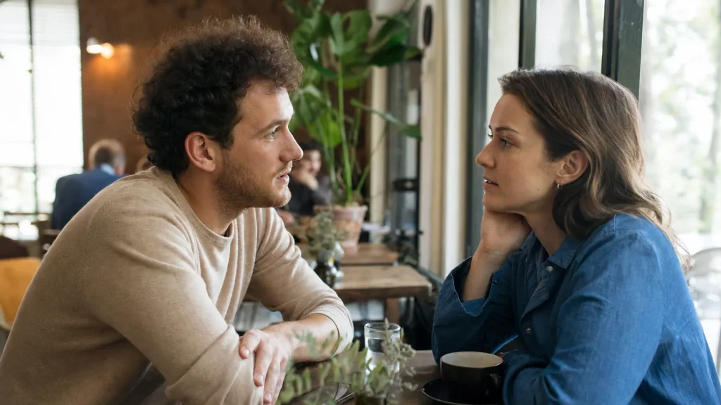 Two adult friends discussing a possible romantic relationship during a low-pressure daytime café meeting.